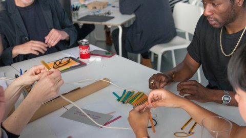 Photo of people working together around a table making things with string and lollipop sticks and more
