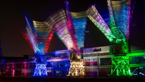 Photo of 3 cranes on Bristol harbourside at night, lit up by multi-coloured lights lights