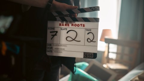 A film clapboard displaying "BARE ROOTS," scene 7, slate 22, take 2, with details for director, DOP, and date visible.