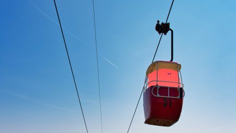 A coral coloured barrel like character sits in a cable car with a beautiful landscape behind it in Llandudno.