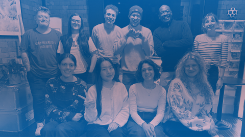 Ten people pose together and smile in front of a wall.