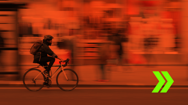 Photo of a cyclist passing by a blurred background of city shops, all overlayed with a red filter
