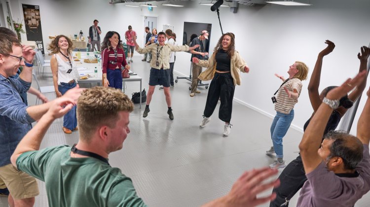 People are standing in a cirlce, some jumping, with arms in the air smiling