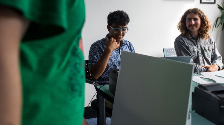 A casual meeting in a modern office setting, featuring three individuals engaged in discussion around a glass table.