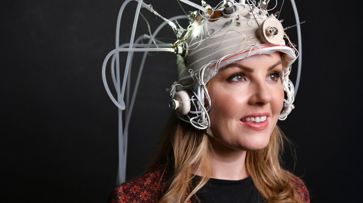 A woman holding a microphone wears an elaborately designed helmet