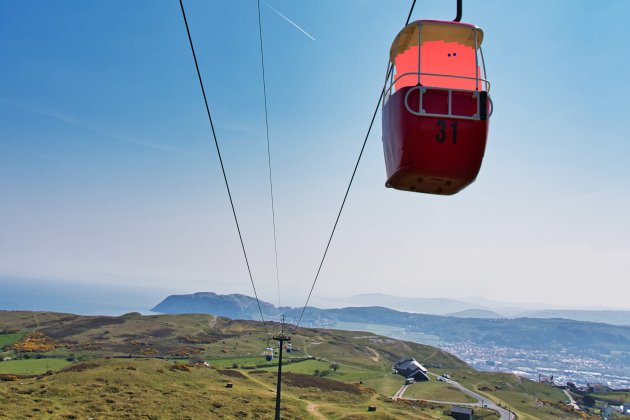 A coral coloured barrel like character sits in a cable car with a beautiful landscape behind it in Llandudno.