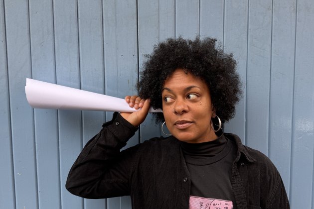 A photo of a woman holding a paper cone up to her ear as if she is listening to it.