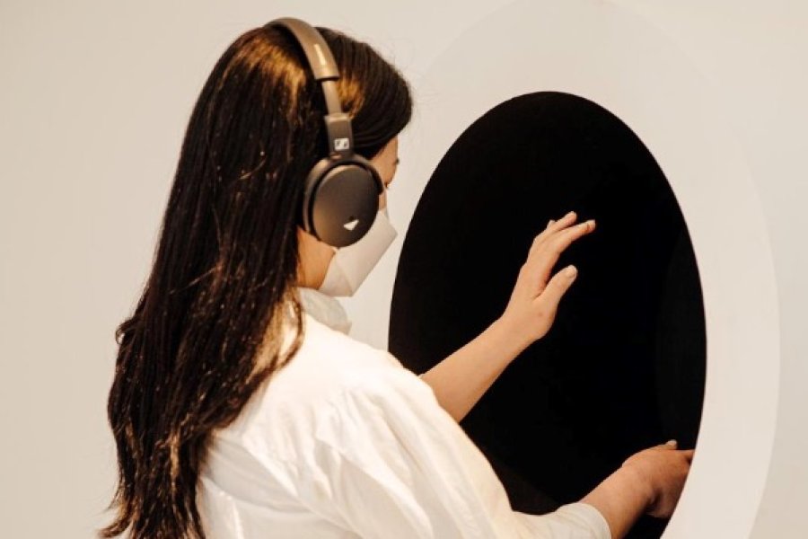 A woman wearing headphones and a mask stands before a black hole, feeling what's inside.