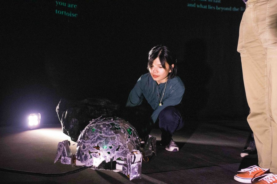 Image of robotic tortoise interacting with the artists in a dimly light room.
