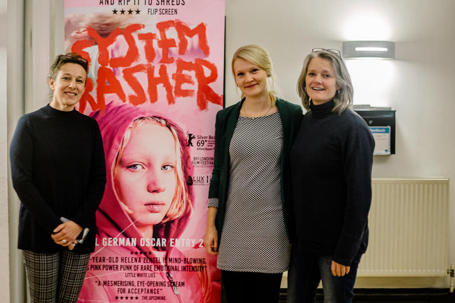 Three women standing with a cinema poster smiling