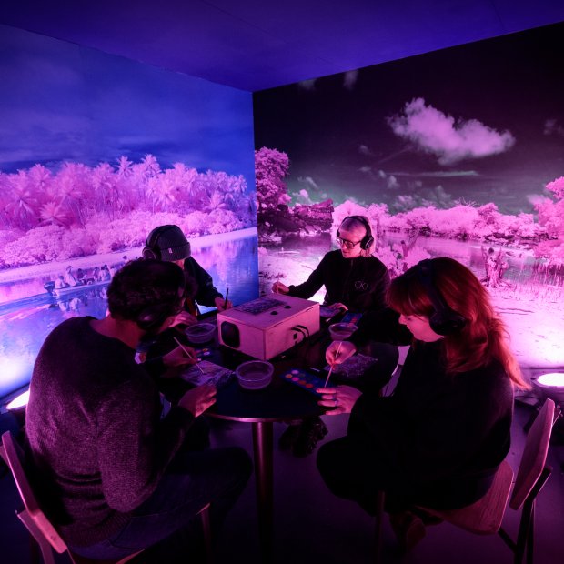 Four people take part in an immersive experience, they are wearing headphones and painting with watercolours.