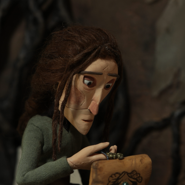 A character with brown hair in a green outfit holds a small wooden box, surrounded by a dark, textured background.