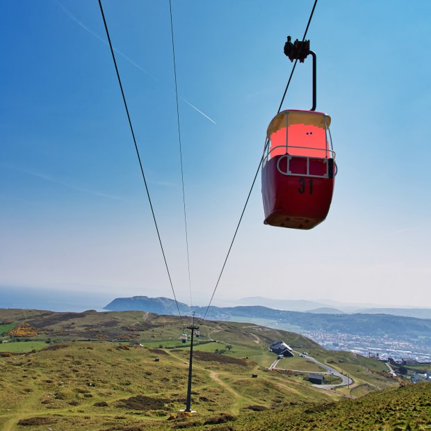 A coral coloured barrel like character sits in a cable car with a beautiful landscape behind it in Llandudno.
