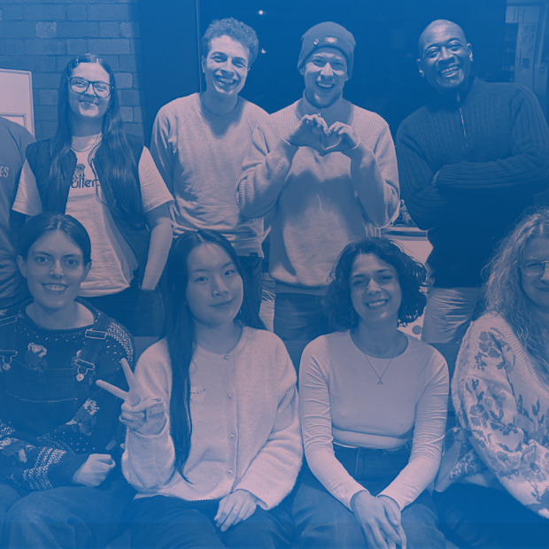 Ten people pose together and smile in front of a wall.