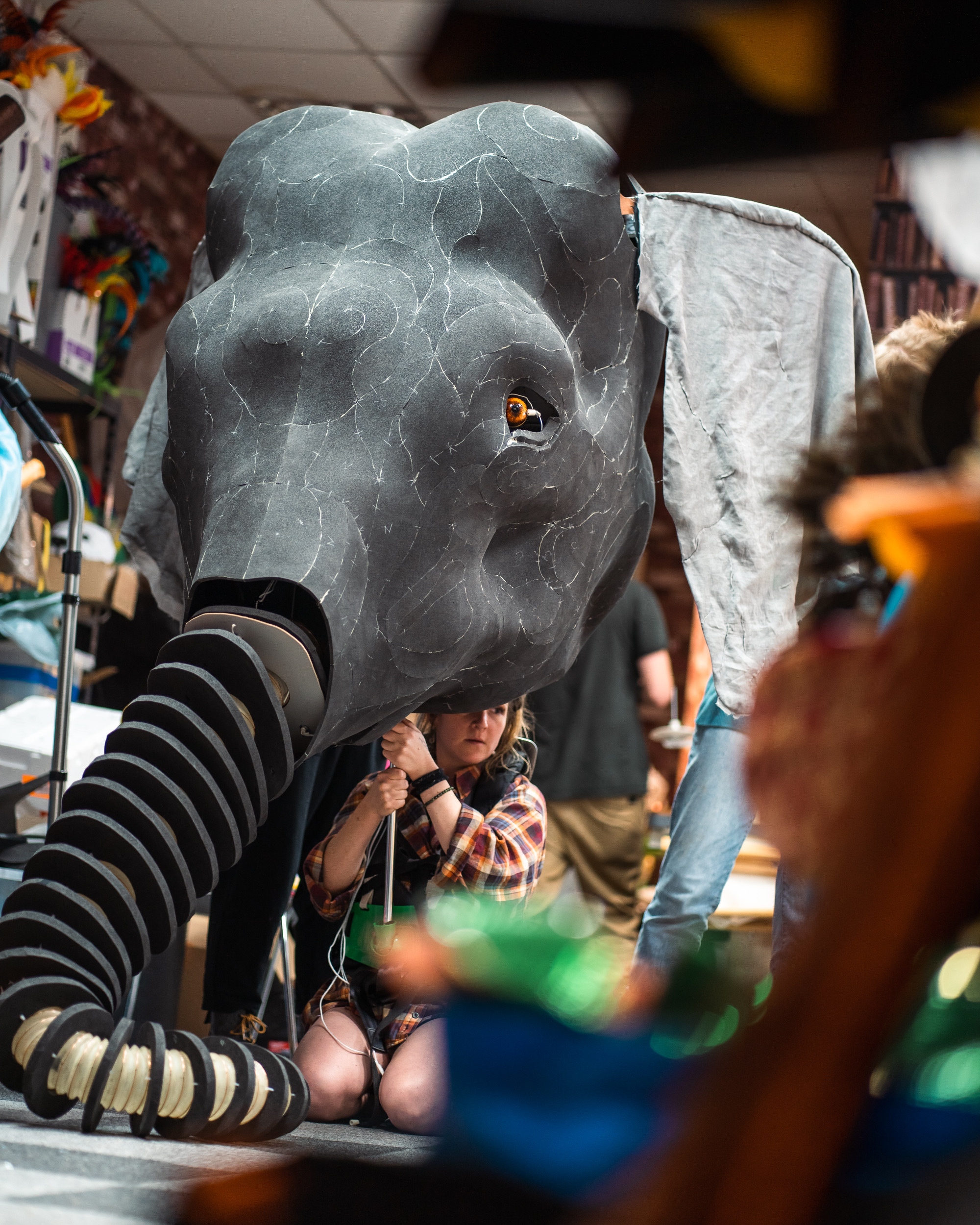 Hannah sitting on the floor holding a giant elephant puppet on a pole