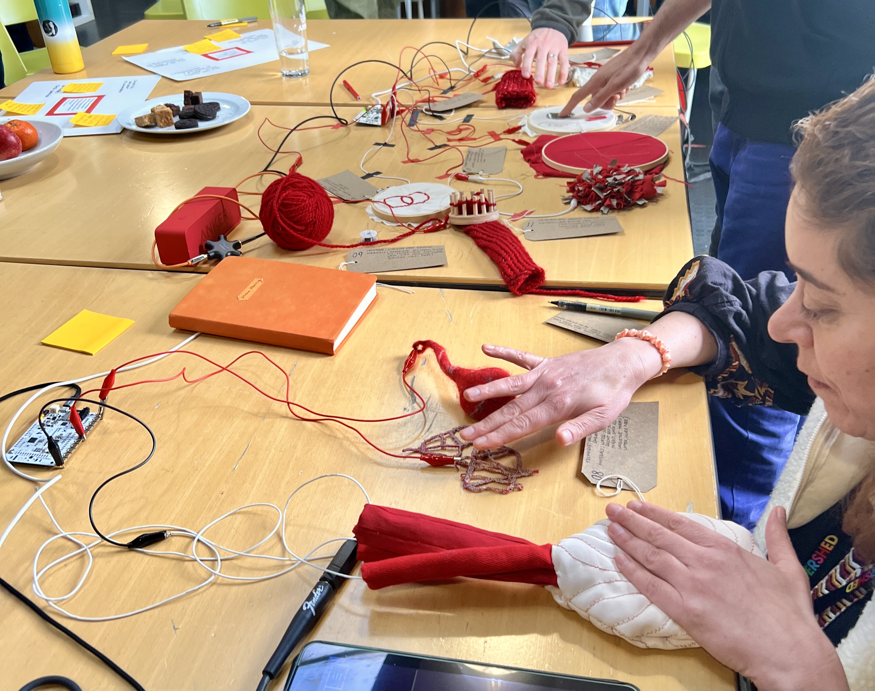 A selection of red and white electronic textile samples on a beige/brown table. In the foreground is a person touching two of the samples with two other people touching samples in the background