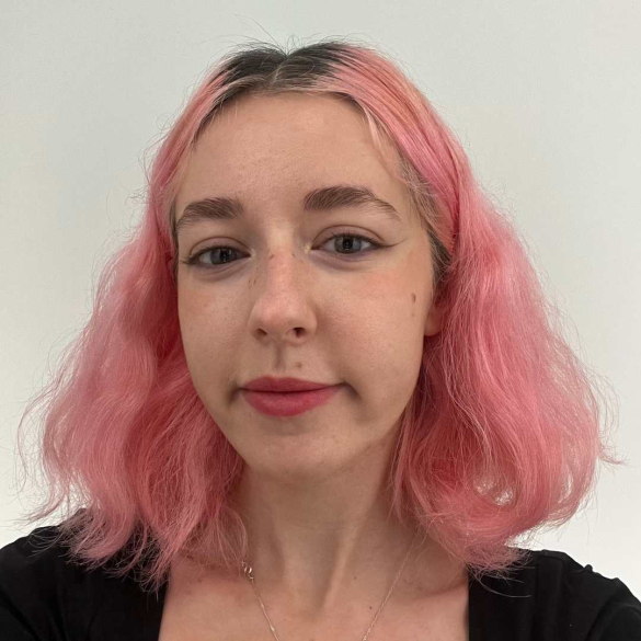A young woman with white skin and pink wavy hair looks straight into the camera.