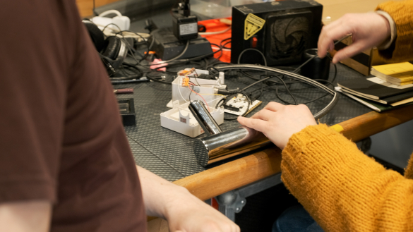 Geraint and a member of the studio team collaborate on a workbench, examining and assembling electronic components with tools and cables scattered around
