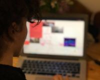 The back of a woman's head as she designs a zine on her laptop screen.
