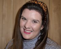 An image of Liz's head and shoulders. She is a white woman and is smiling. She has long brown straight hair and is wearing a leopard print headband and a fuzzy purple jumper.