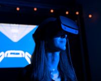 Image of a woman wearing a VR headset with the image of a hospital bed projected in the background