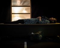 Woman lying down on a platform. Lamps glowing behind. Image by Jon Aitken