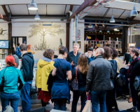 People gathered in a group and talking. In the background there is a black and white illustration on the wall