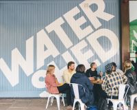 Image of a group of people sat in front of the undershed - in the background is a blue wall with 'Watershed' in white letters