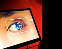 An image of a TV screen, in front of a red wall. On the screen is a close up of someones eye, over the top of the eye is a a graphic that appears to be scanning the blue iris of the eye