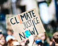 Photo of a cardboard placard at a climate rally saying Climate Justice Now
