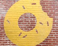 An image of a spray painted yellow doughnut on a brick wall