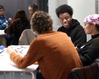 3 people sit around a table, they are happily in discussion. 