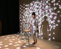 Photo of a person stood in front of a screen with a projected image on their body and the screen