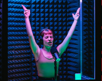 a woman in a sound booth with headphones with raised arms