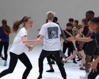 People of varying ages take part in a movement based activity in a large space.