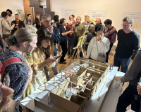 A photo of a group of people looking at a scale model of a building interior and socialising