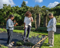 Three people stand outdoors looking at the ground, grass covered by tarpaulin