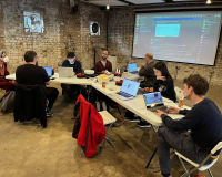 An image of of various people at a shared desk in a triangle formation, working on creative projects collaboratively.