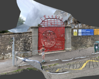 An image of a red gate sidelined by grey walls on either side, by a littered road. 