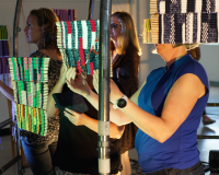 3 people explore woven tapestries suspended from a metal frame