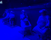 Three older adults test VR headsets in a darkened, blue room.