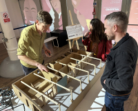 Three people gather around a wood and cardboard model of Undershed, the Watershed's new immersive gallery space.
