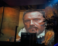 An image of an AI Generated picture of William Shakespeare projected onto a building at night time. 