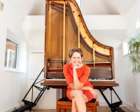 An image of pianist Sarah Nicolls sat in front of her Future Piano, which resembles an open piano positioned on its front. 