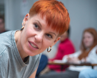A white woman with short dyed red hair looks away from the camera