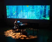 someone playing piano next to a large blue screen