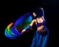 Image Shrouk El-Attar belly dancing in drag, with a rainbow coloured piece of cloth mid dance.