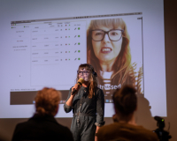 Photo of Victoria Melody holding a mic talking to an audience.