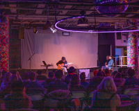 Image of Craig Scott performing on the semi-automated guitar to a small crowd of seated people