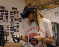 Woman in a VR headset holding controllers in a room full of posters and images on the wal
